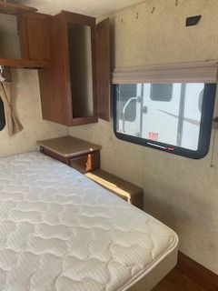 A white bed, small cabinets, window and open drawer.