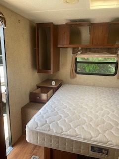 Bedroom in RV with bed, small cabinets, window and open drawer.