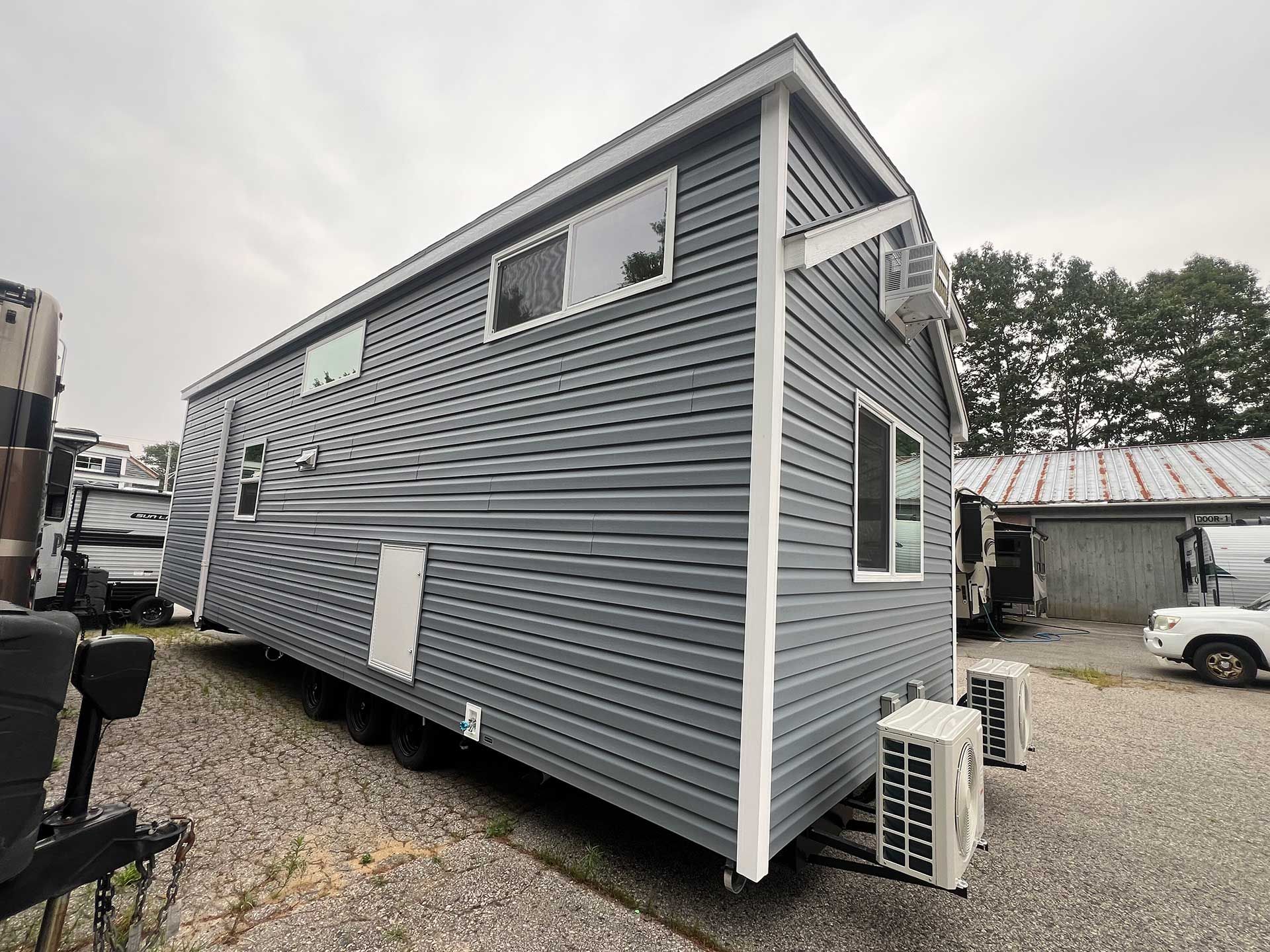 tiny gray house with white trim, two AC units outside, parked outdoors