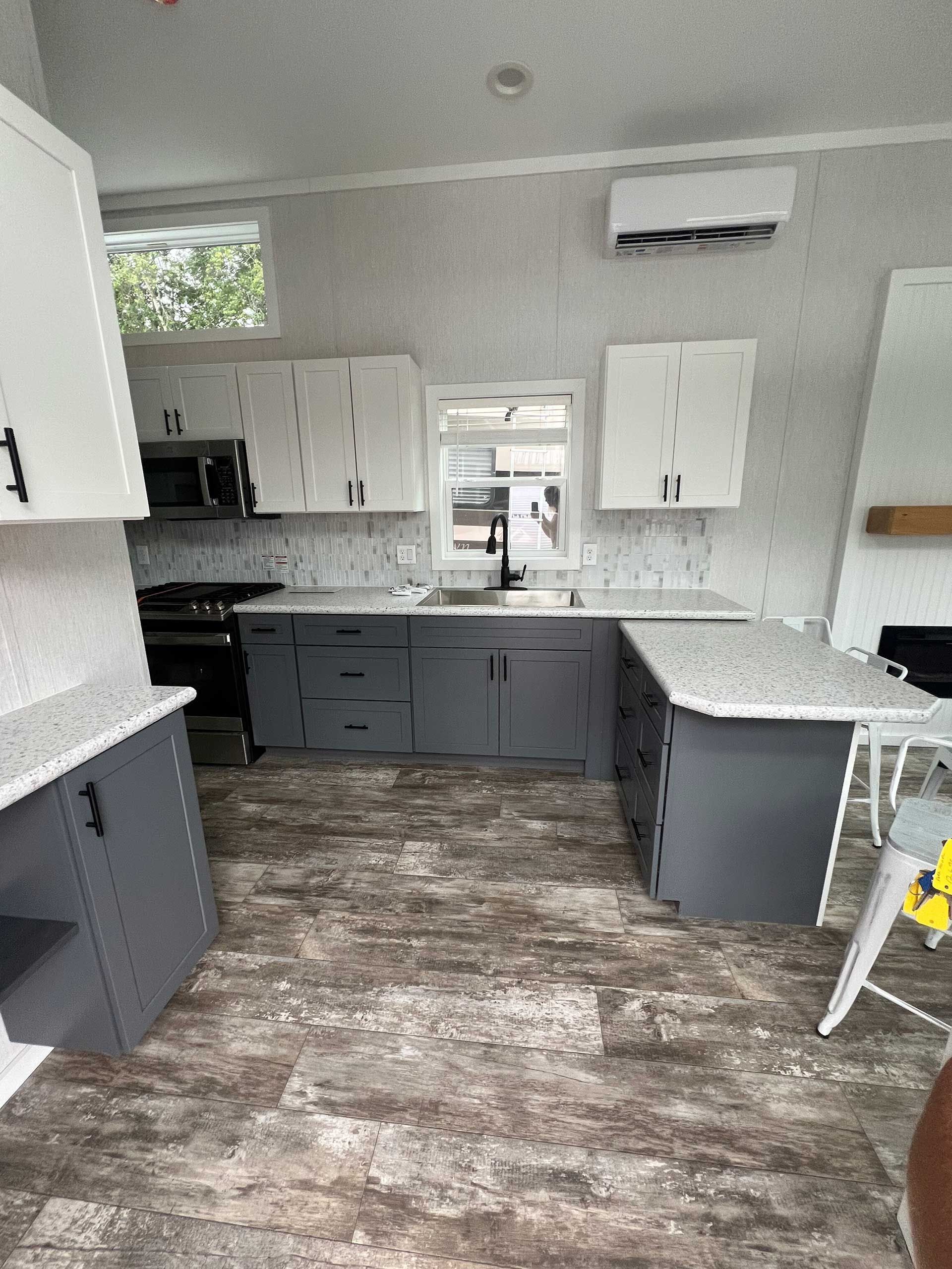 a modern kitchen with gray and white cabinets, granite countertops, and dark appliances in a neutral-toned space
