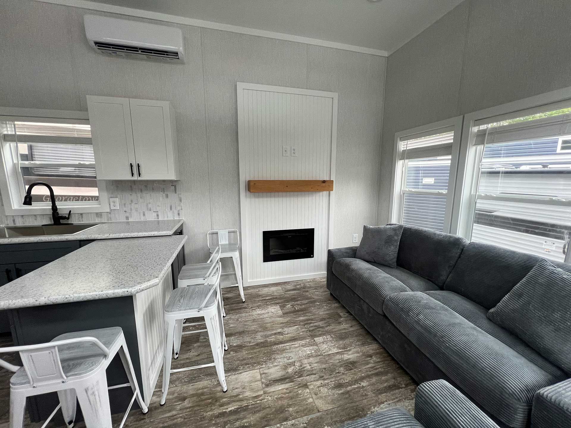 interior of a small living space, kitchen with bar stools, fireplace, and a couch with a waterfront view