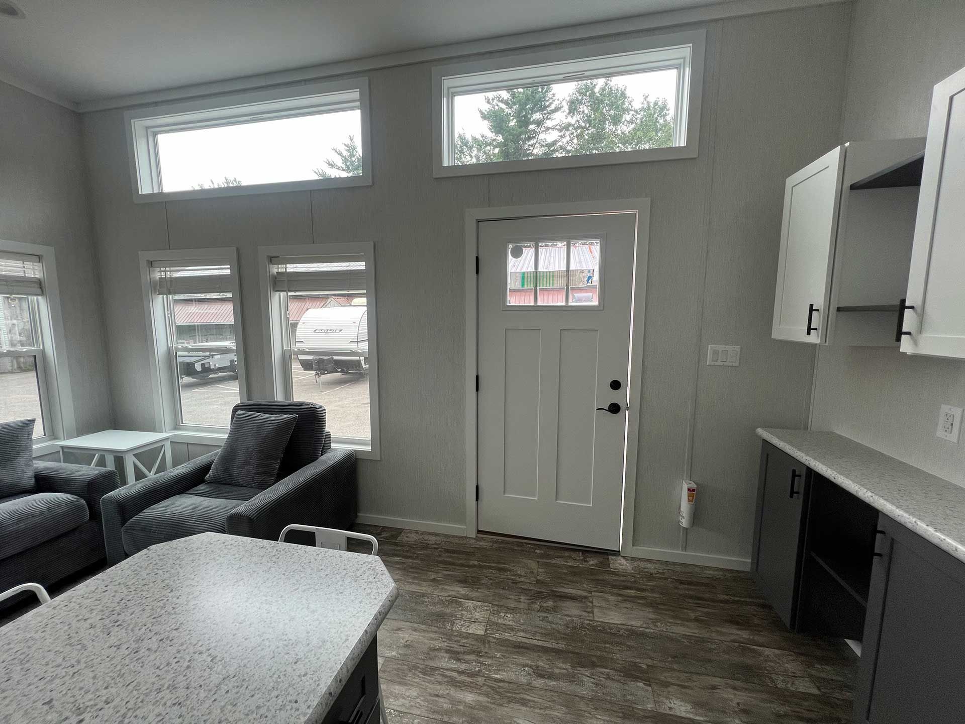 living area with grey seating, kitchen, door, and windows; gray walls and flooring