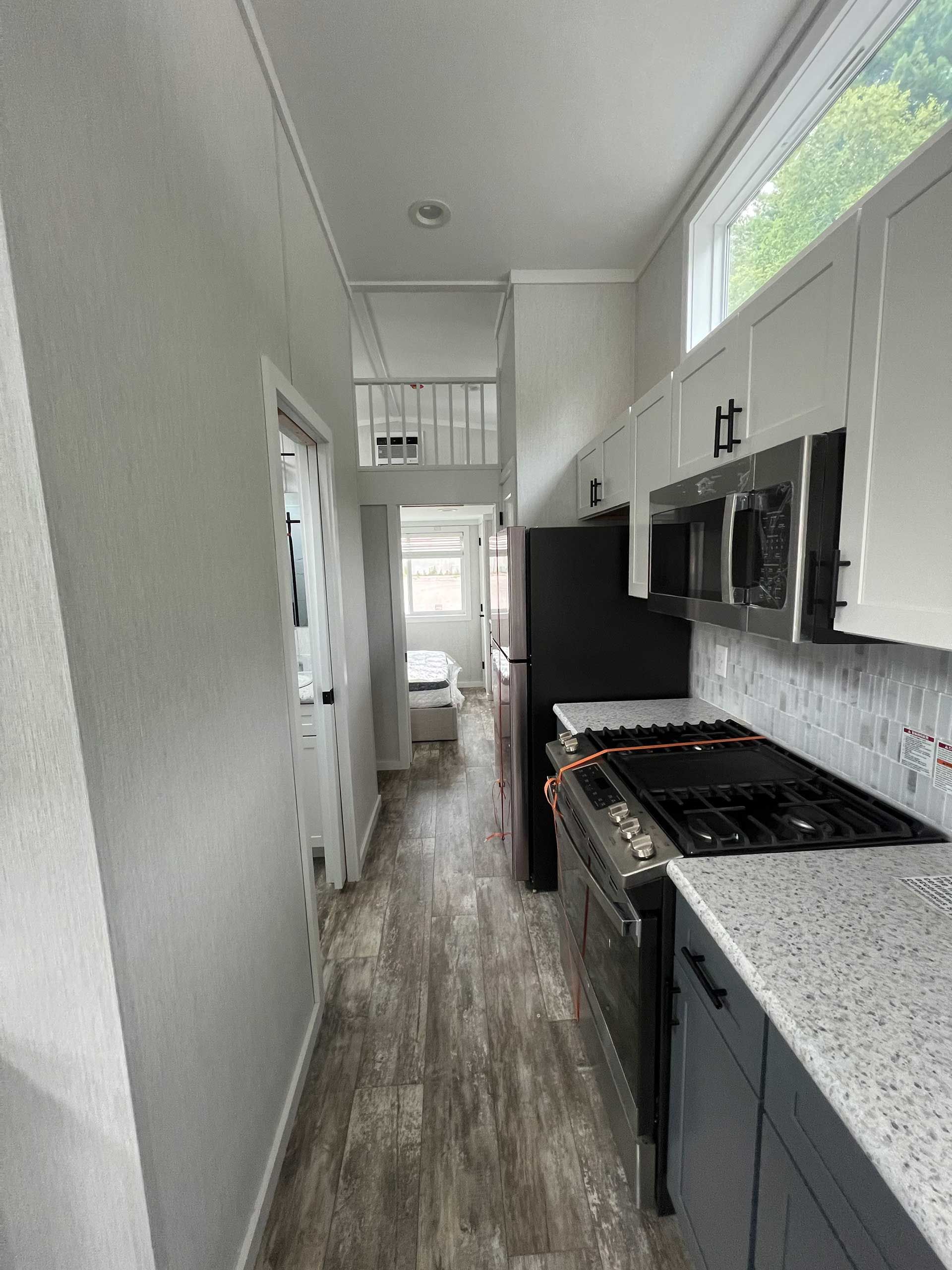 narrow kitchen in a tiny home; light gray walls, dark cabinets, appliances, and wood-look flooring