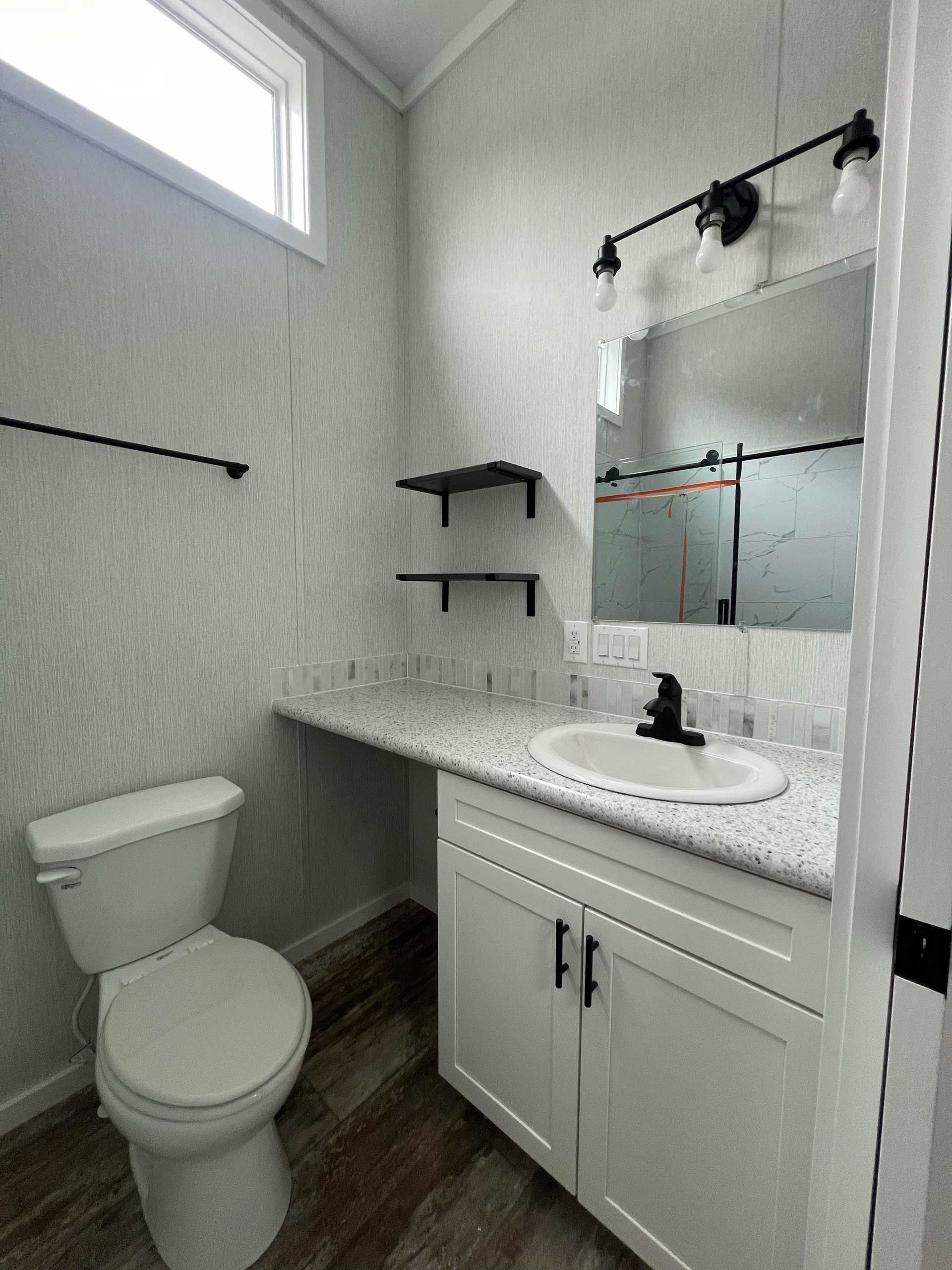 bathroom with white toilet, sink, cabinets, and black fixtures, light-colored walls and flooring