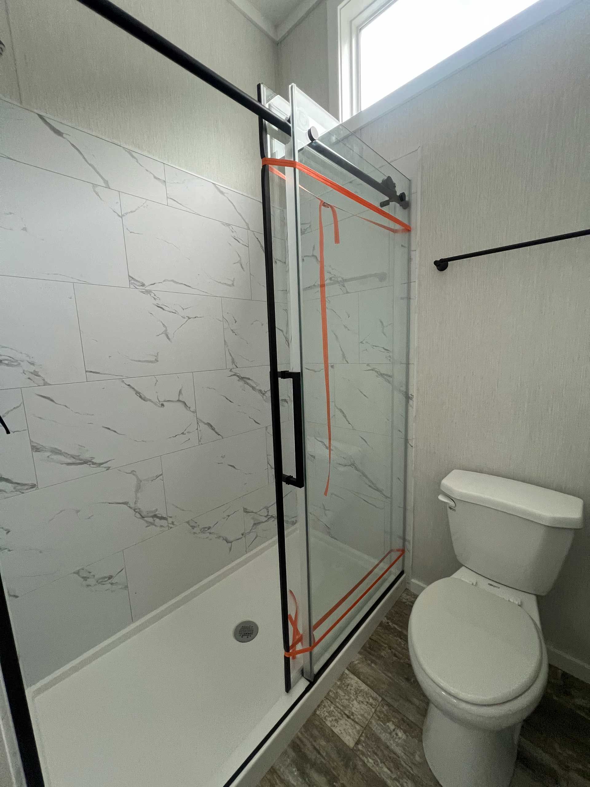 bathroom with a marble-look shower, black sliding glass door, and a toilet