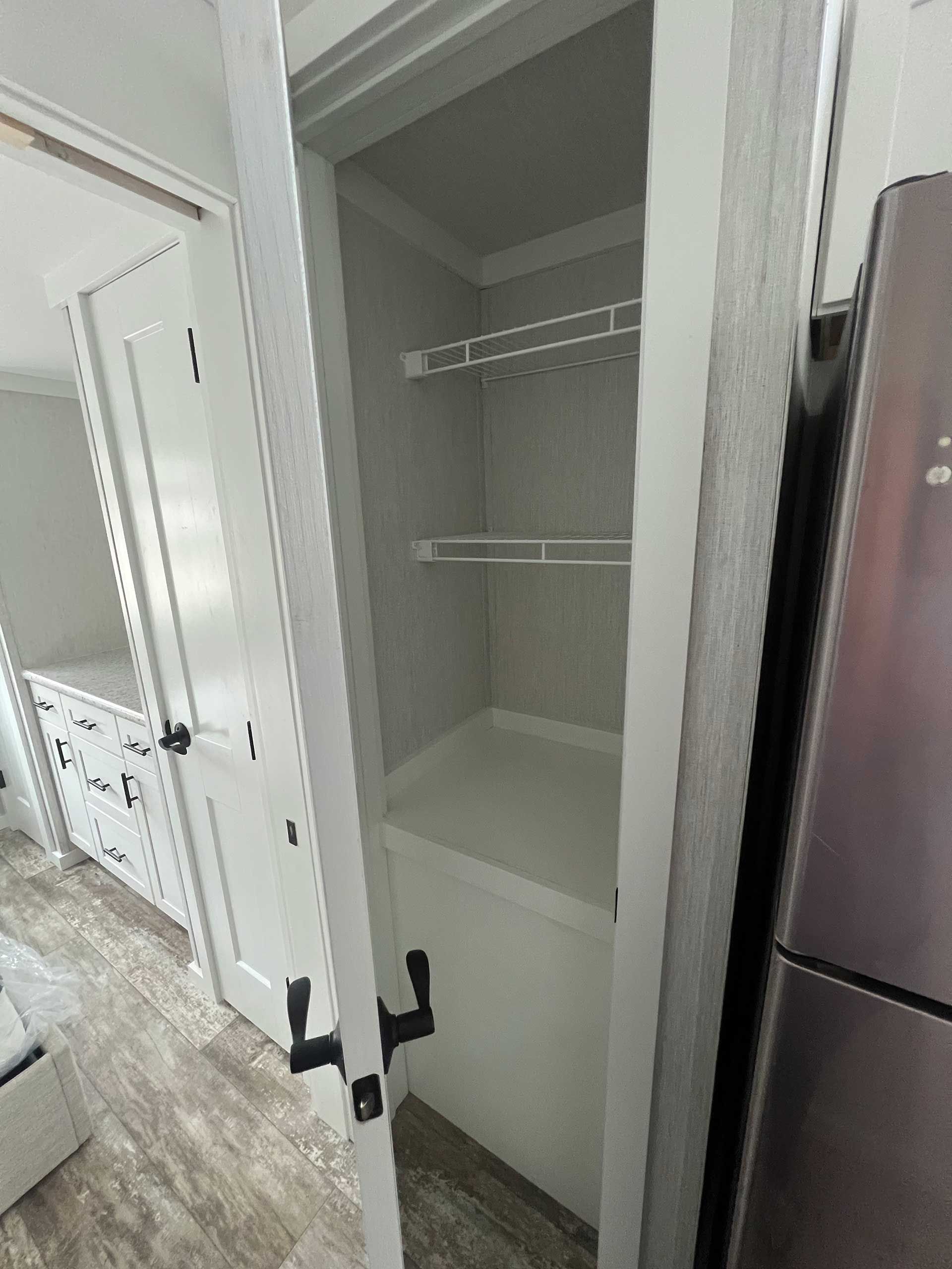 a narrow white pantry with wire shelves and a solid bottom shelf, next to a refrigerator