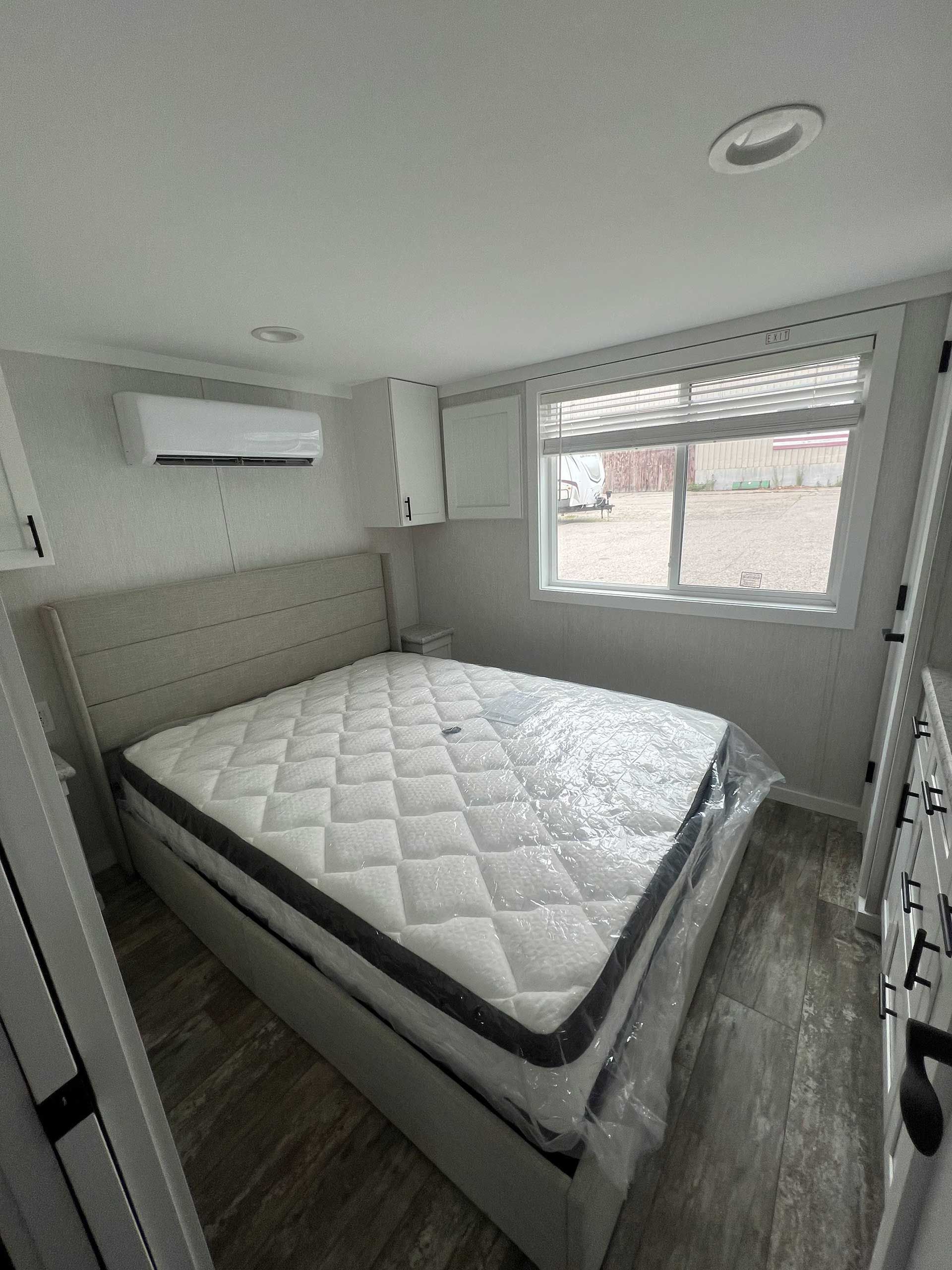bedroom with bed, mattress, window, cabinets, air conditioner; gray and white colors