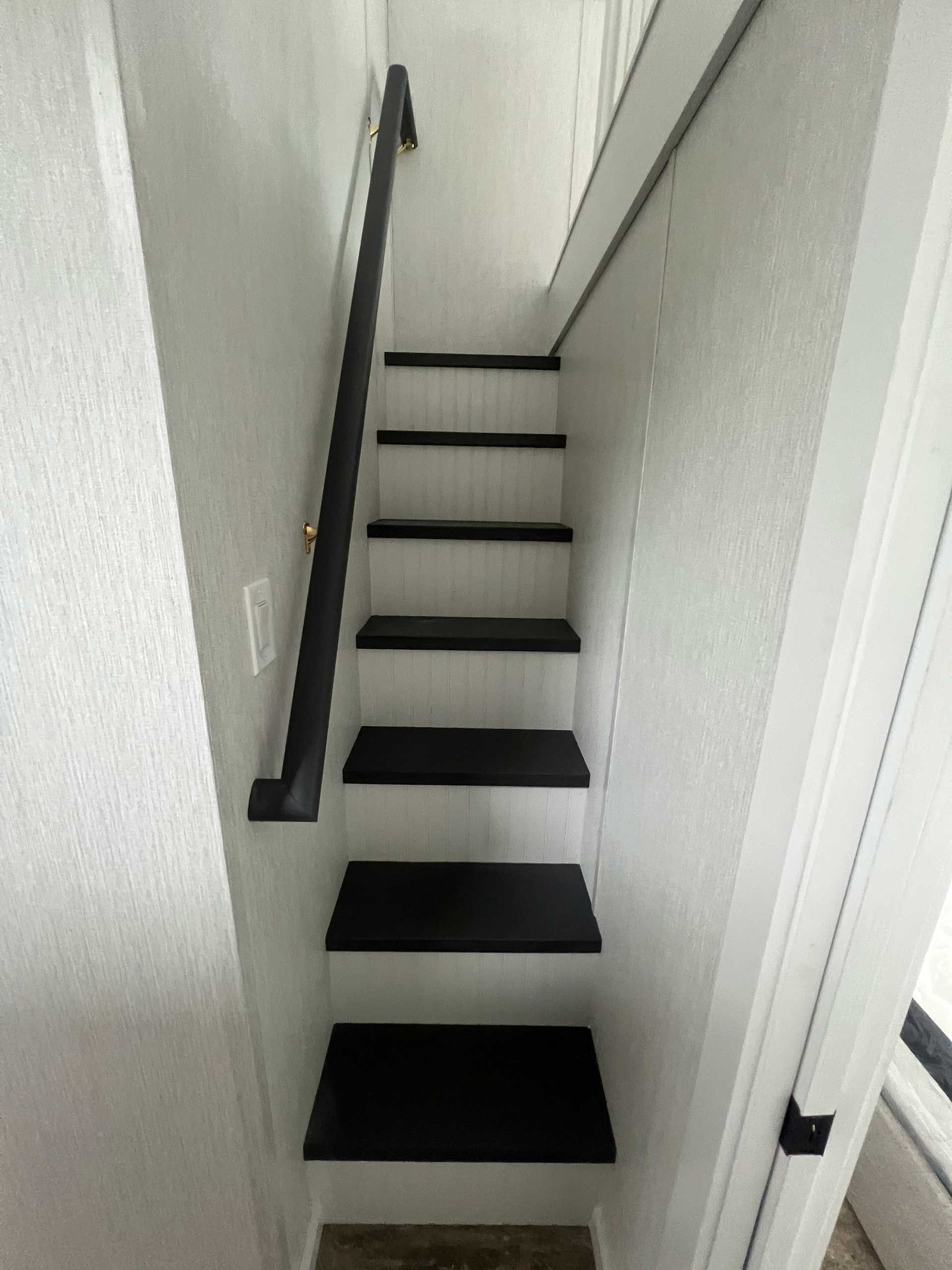 narrow, black and white staircase with black handrail ascending