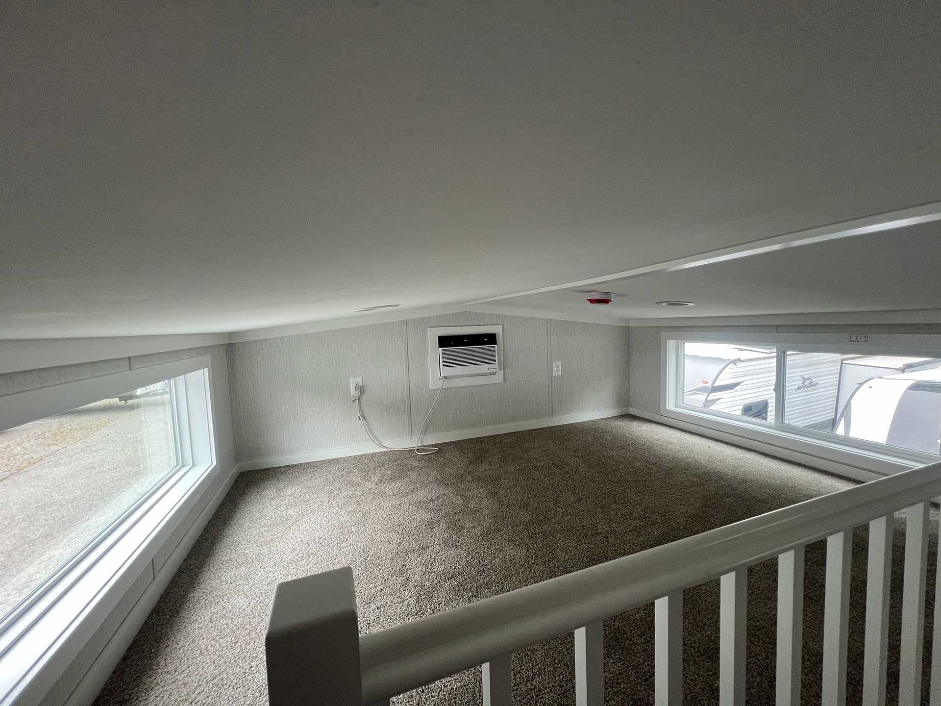 interior loft of a tiny home, carpeted floor, windows, railing, air conditioner