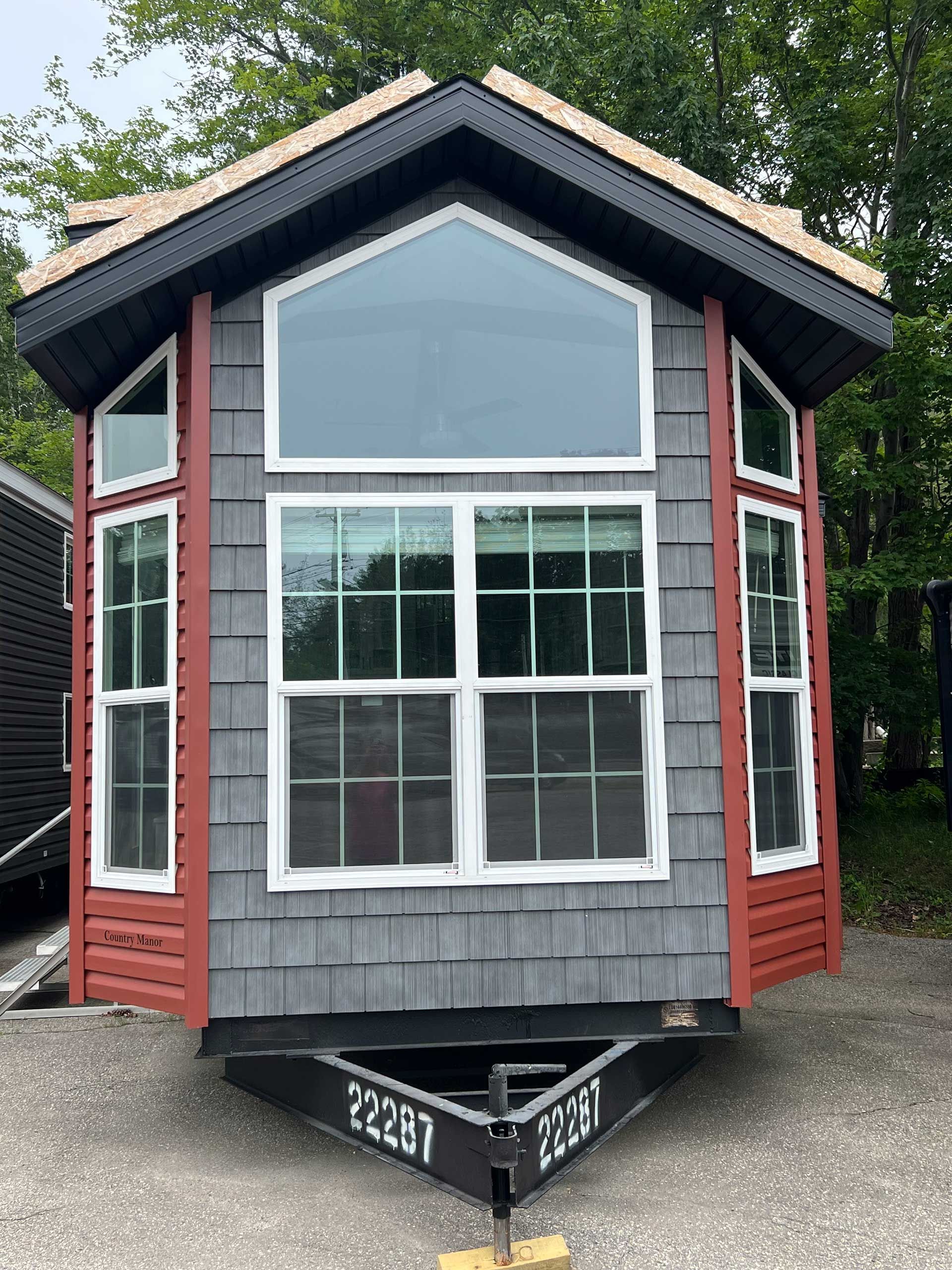 tiny red-gray cabin on trailer with large windows, black roof, and trailer