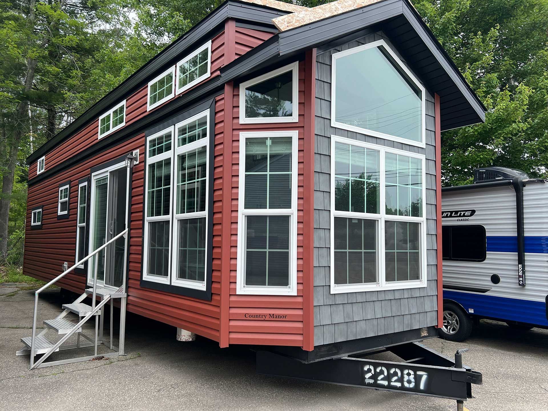 tiny red and gray house on wheels with many windows, stairs, and a trailer hitch