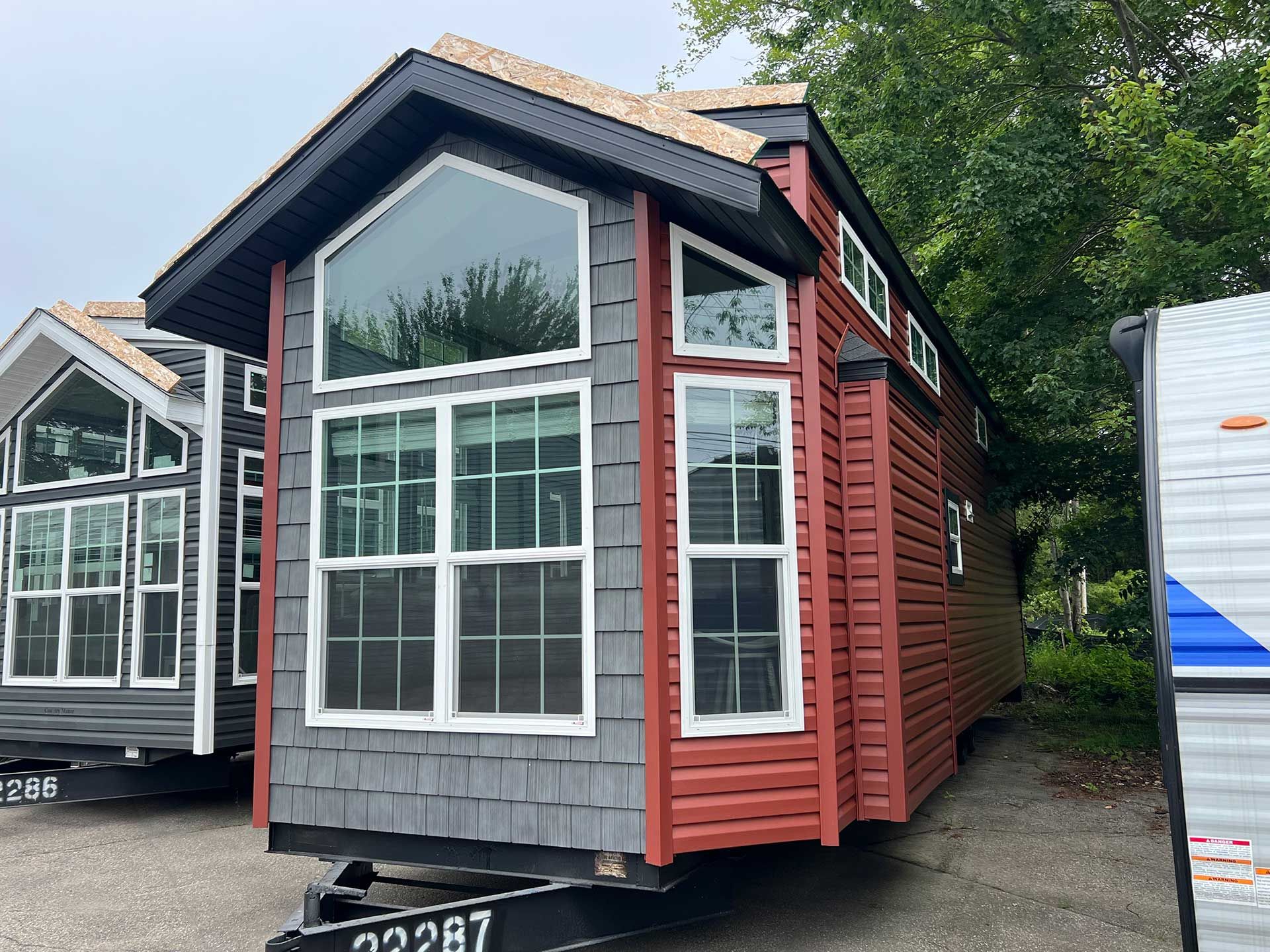 tiny red and gray house on wheels with large front windows; parked outside