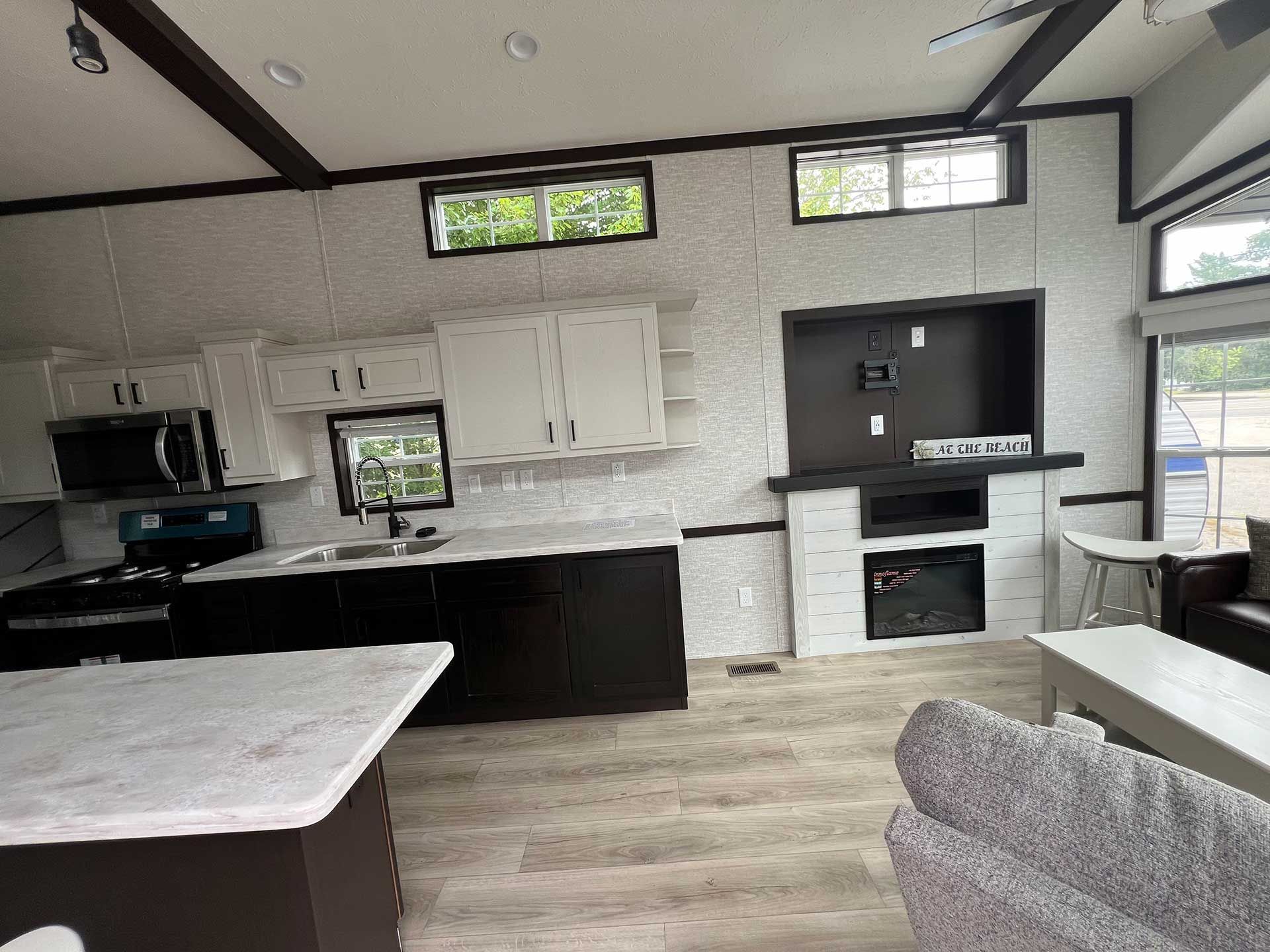 kitchen and living area in a home; white cabinets, black appliances, wood beams, and fireplace