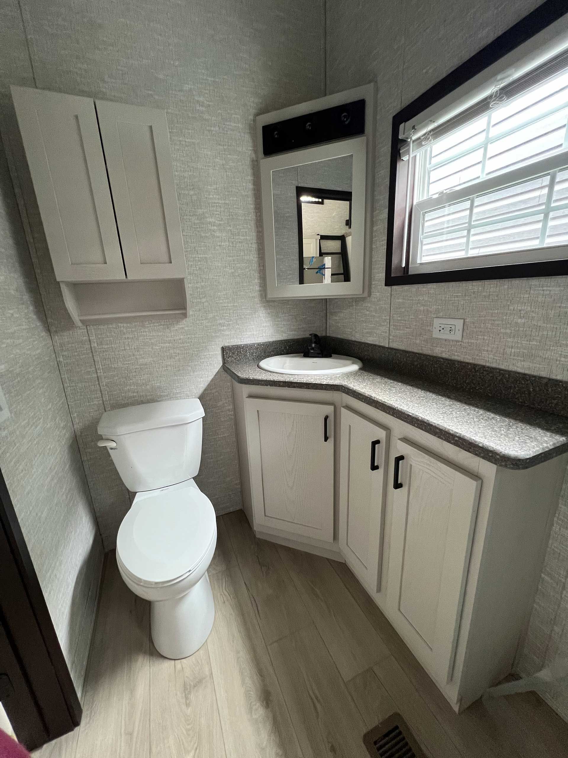 bathroom with a toilet, vanity, and cabinet; light walls, gray countertop, and a window