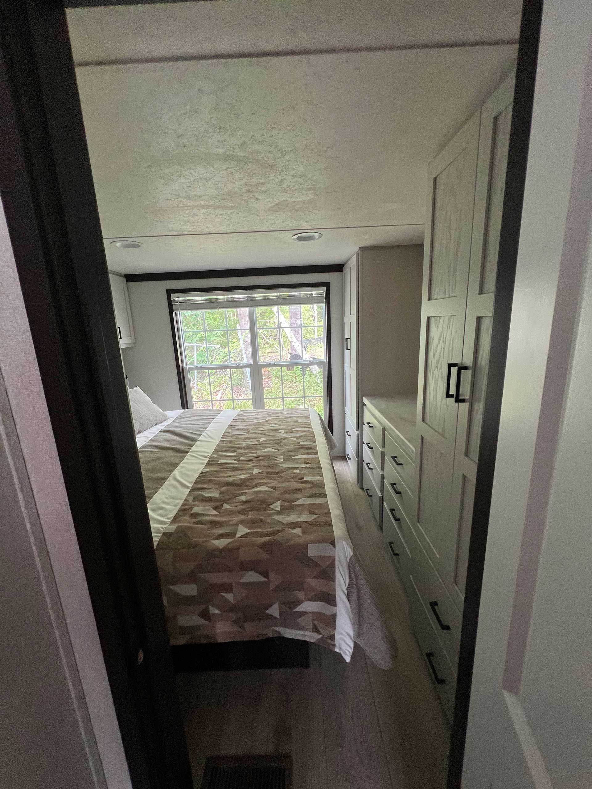 bedroom interior in a camper, with a bed and dresser visible through the doorway