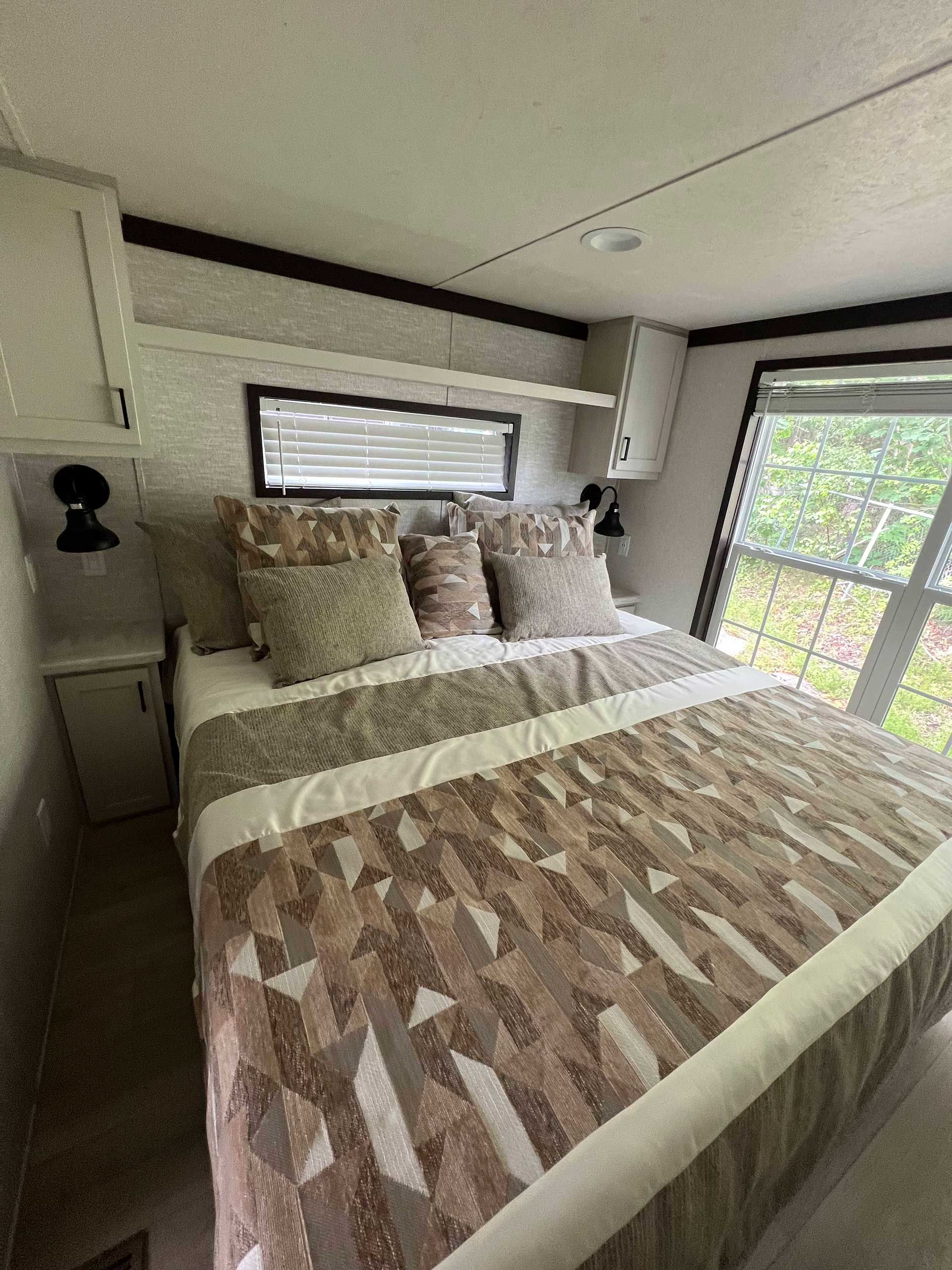 bedroom in a trailer with a patterned bedspread, small window, and cabinets