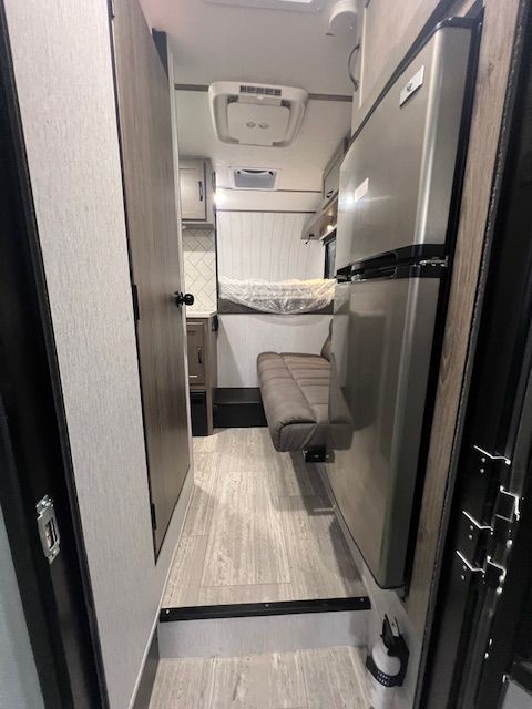 A hallway in a camper with a refrigerator and a bed.