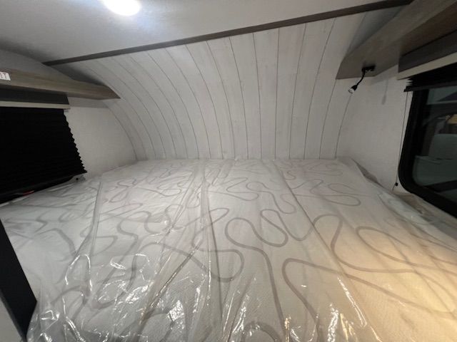 A bed in a camper with a mattress wrapped in plastic.