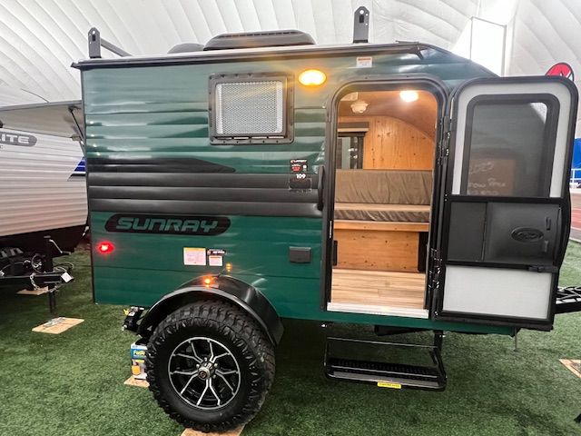 A green trailer with the door open is parked on the grass.