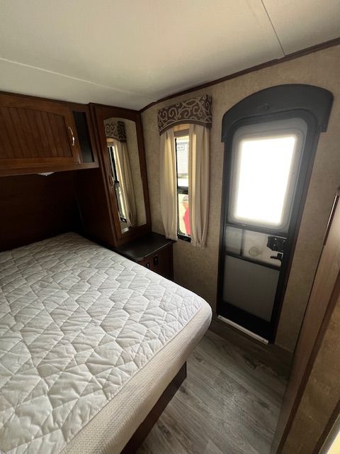 A bedroom in a trailer with a bed and a window.