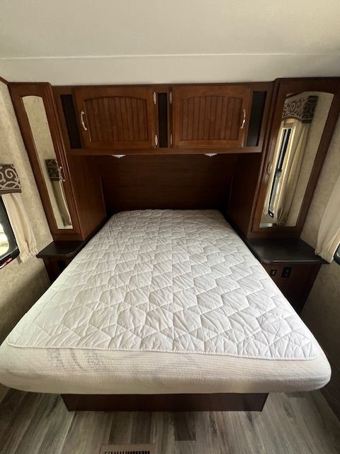 A bed with a mattress and cabinets in a RV.