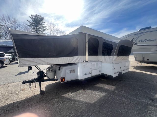 A white trailer with a tent on it is parked in a parking lot.