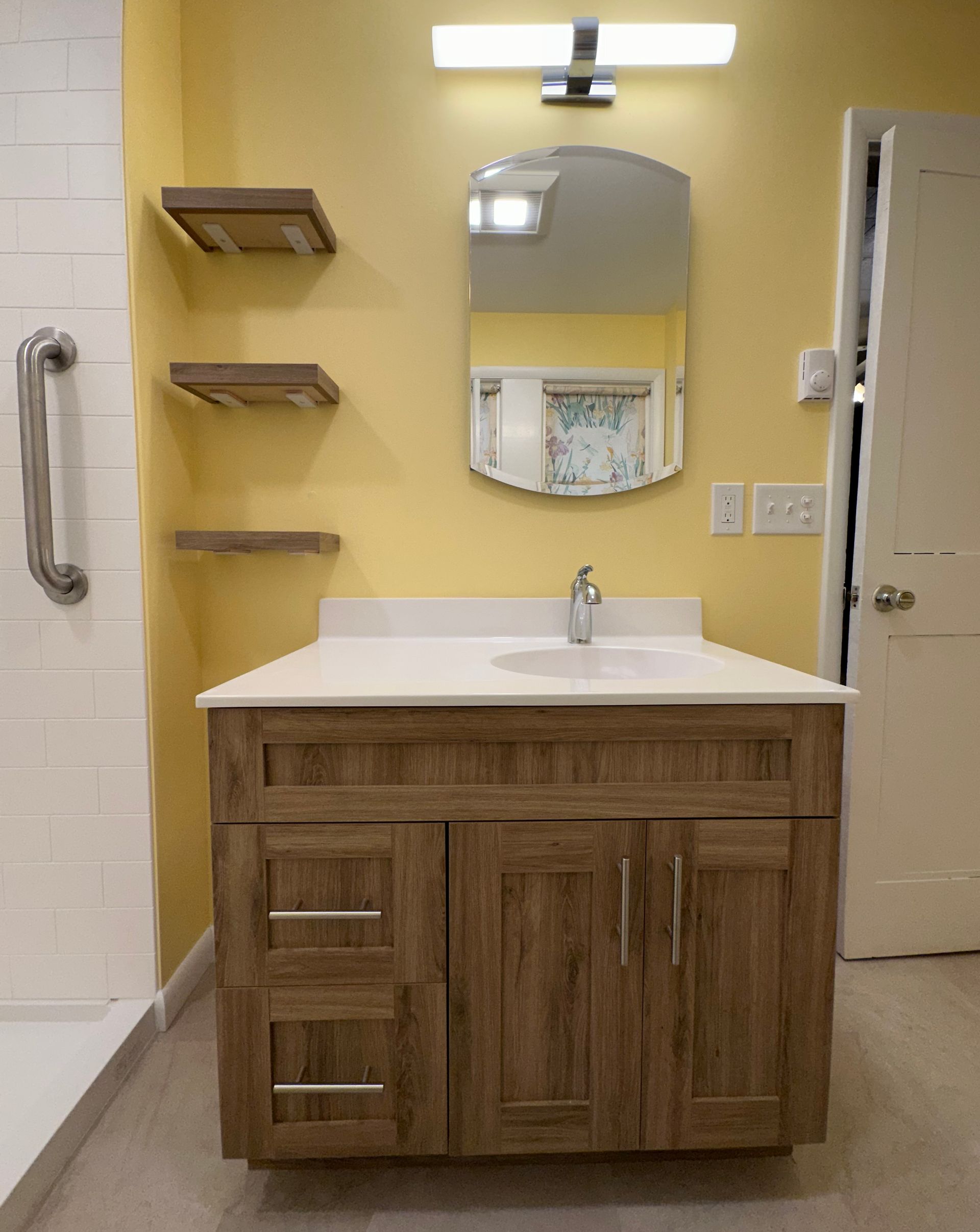 Bathroom with wooden vanity, shelves, and yellow walls. A mirror and light fixture are above the sink.