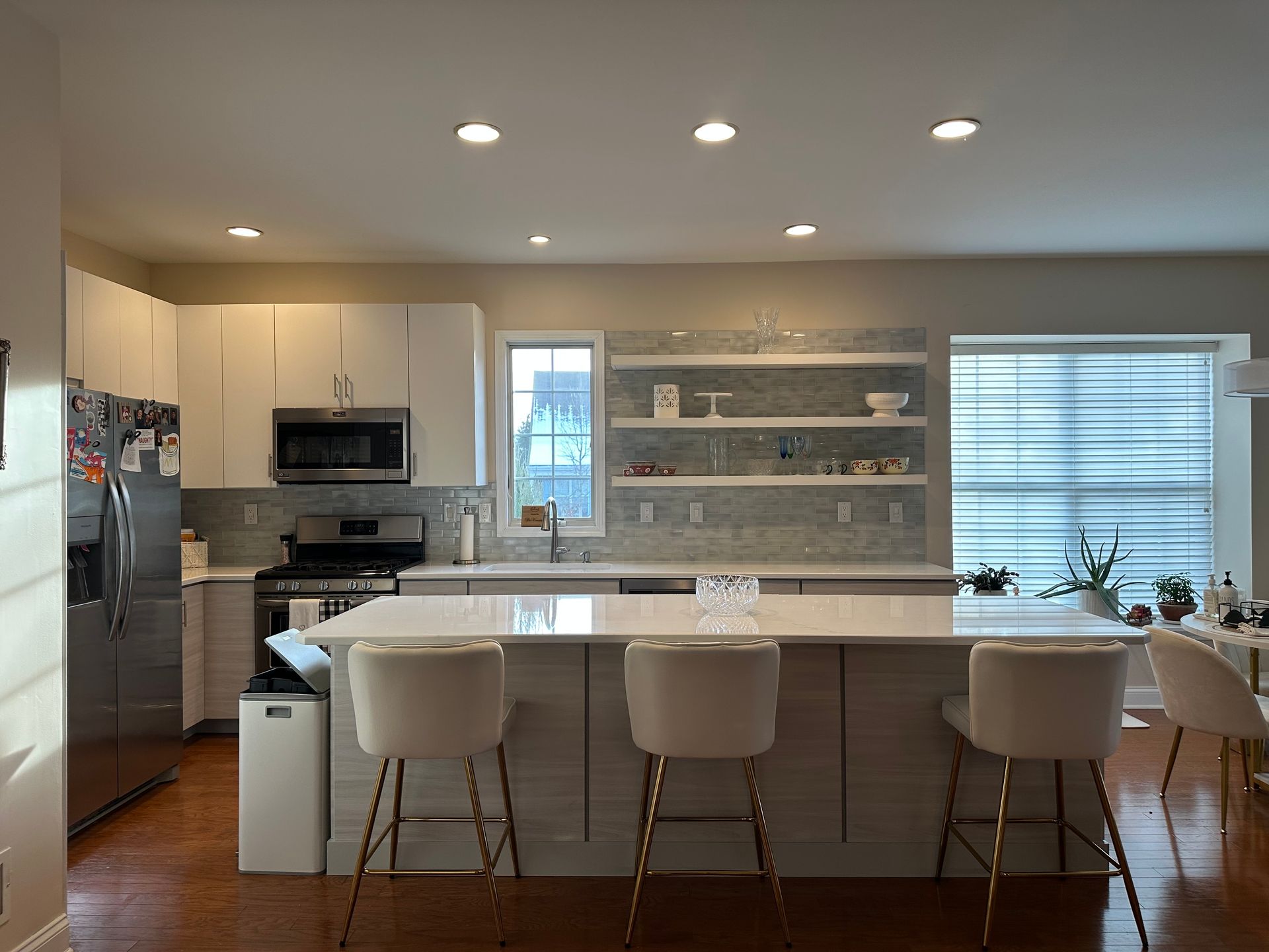 Modern kitchen with white cabinets, island with stools, stainless steel appliances, and wood flooring.
