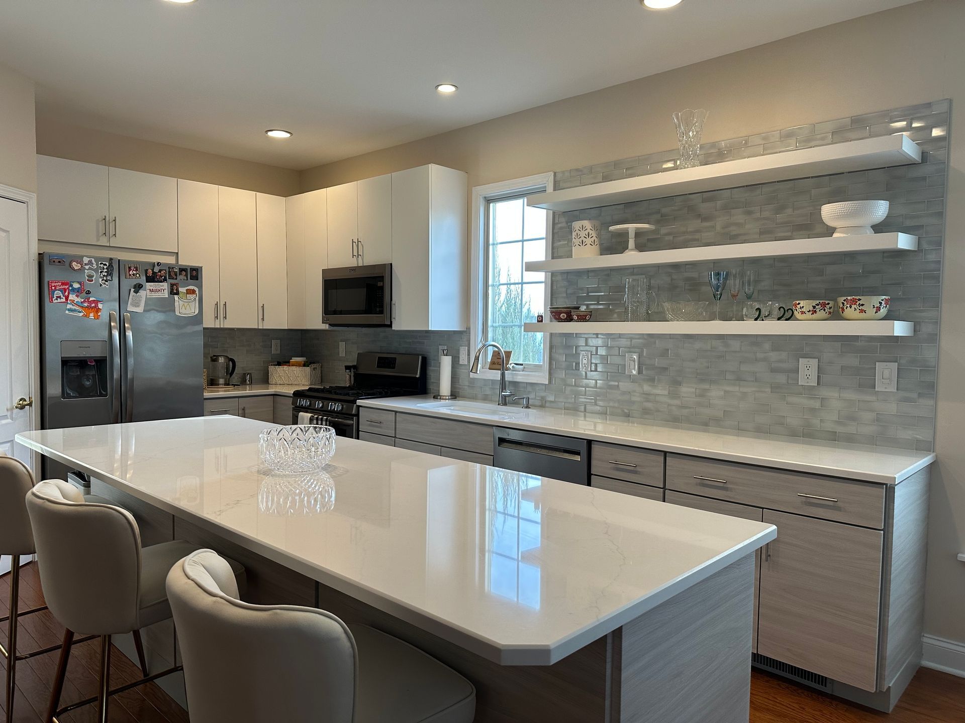 Modern kitchen with island, white countertops, and gray cabinets. Stainless steel appliances and floating shelves.