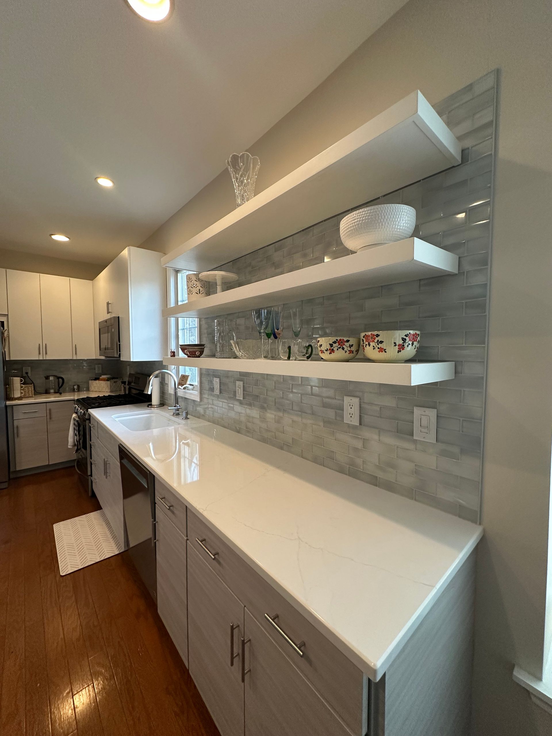 Kitchen with white floating shelves, gray cabinets, white countertop, and gray tiled backsplash.