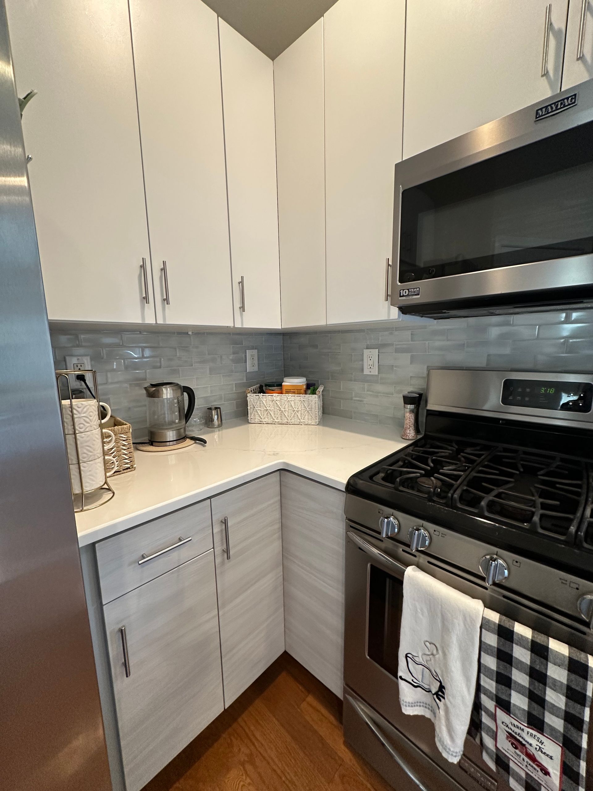 Small modern kitchen with white and grey cabinets, stainless steel appliances, and a gas range.