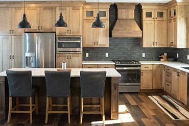 Kitchen with light wood cabinets, dark backsplash, stainless steel appliances, and a central island with bar stools