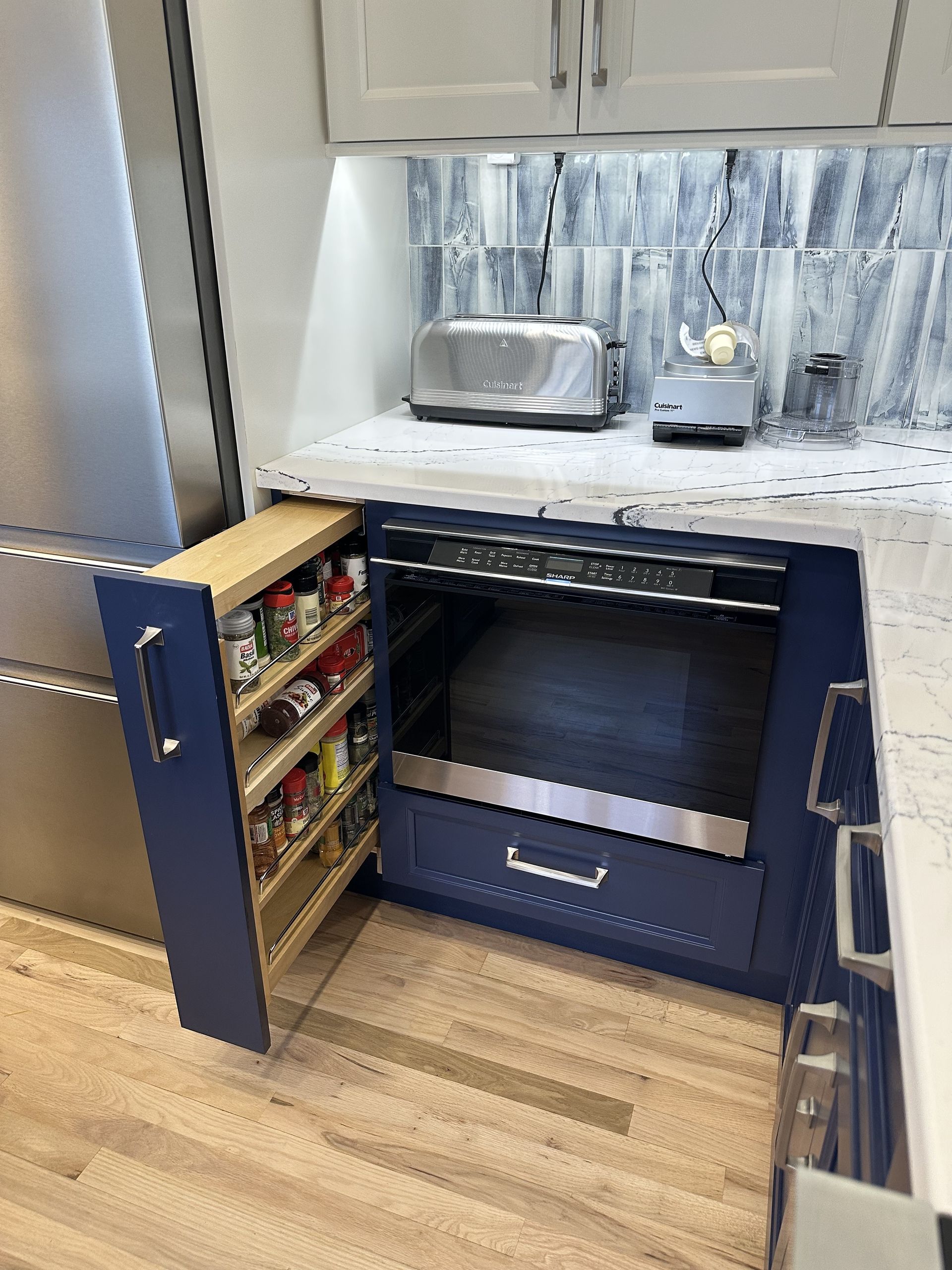 Blue kitchen cabinets with pull-out spice rack next to built-in oven, light countertop, and toaster.