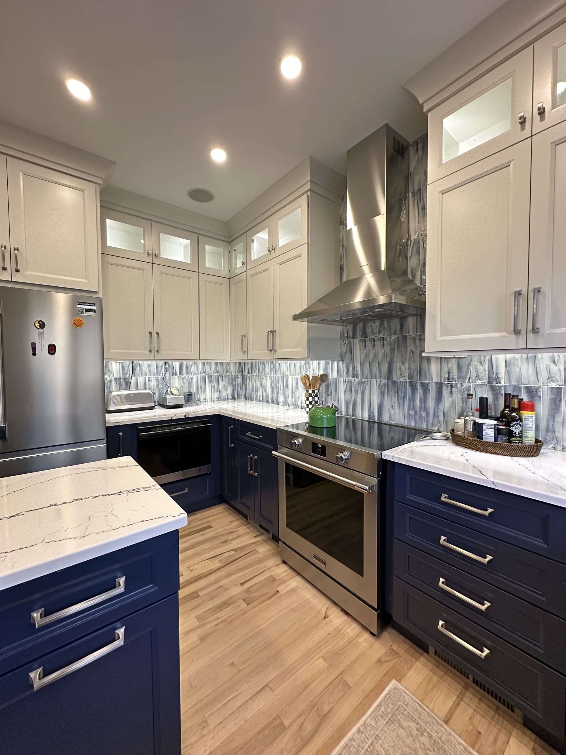 Modern kitchen with blue and white cabinets, stainless steel appliances, and white countertops.