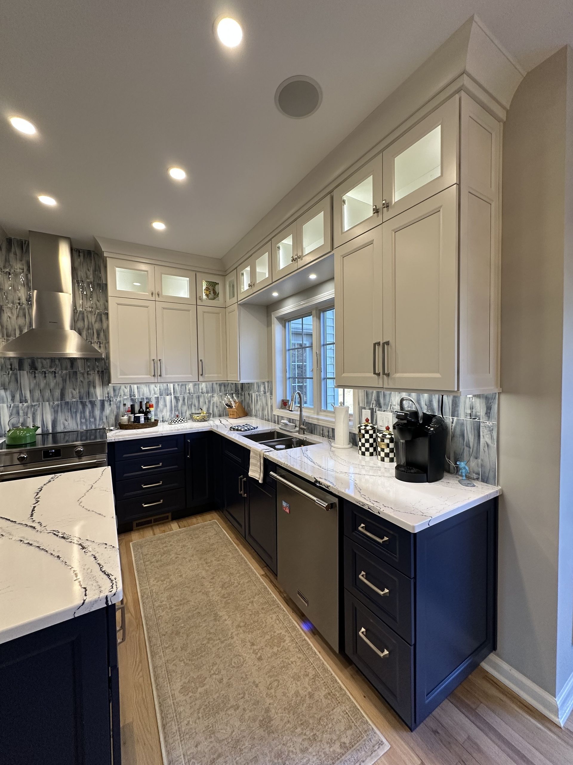 Modern kitchen with blue and white cabinets, white countertops, stainless steel appliances, and a patterned backsplash.
