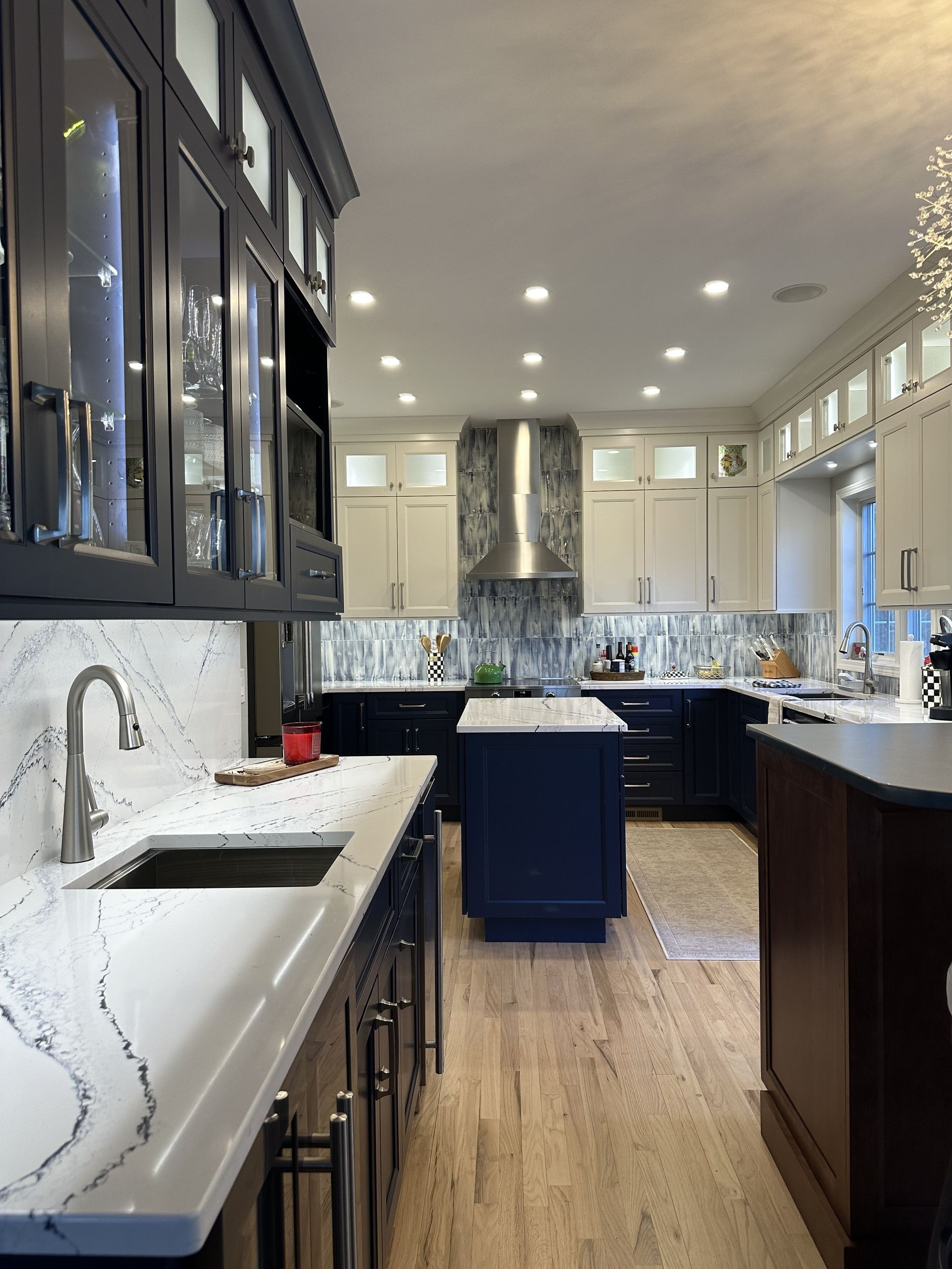 Kitchen with white and blue cabinetry, marble backsplash, stainless steel appliances, and wooden flooring.