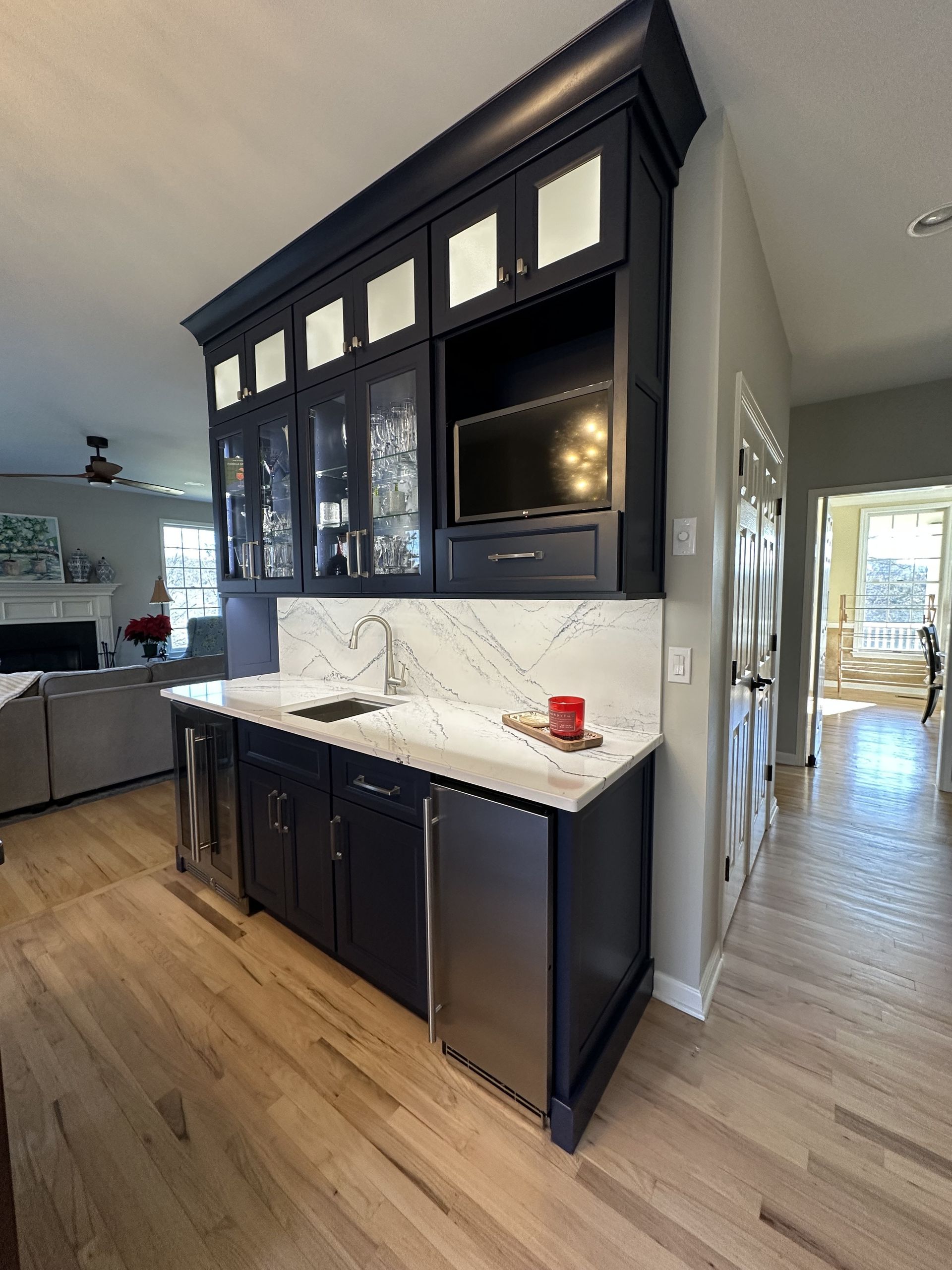 Navy blue wet bar with white countertop and built-in appliances, situated between rooms with a small TV.
