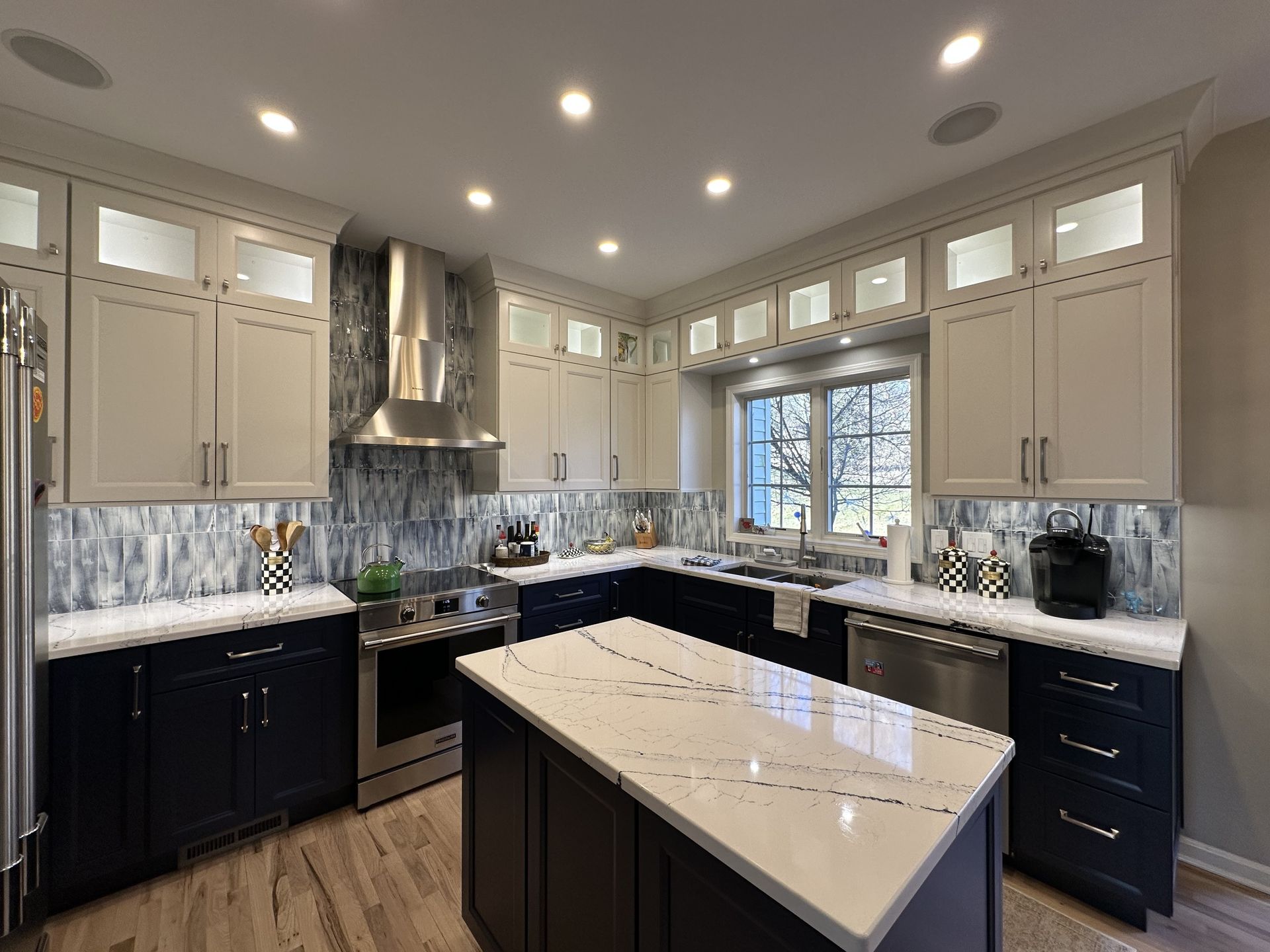 Modern kitchen with two-tone cabinets: blue base, beige upper. Stainless appliances, white countertops, island.