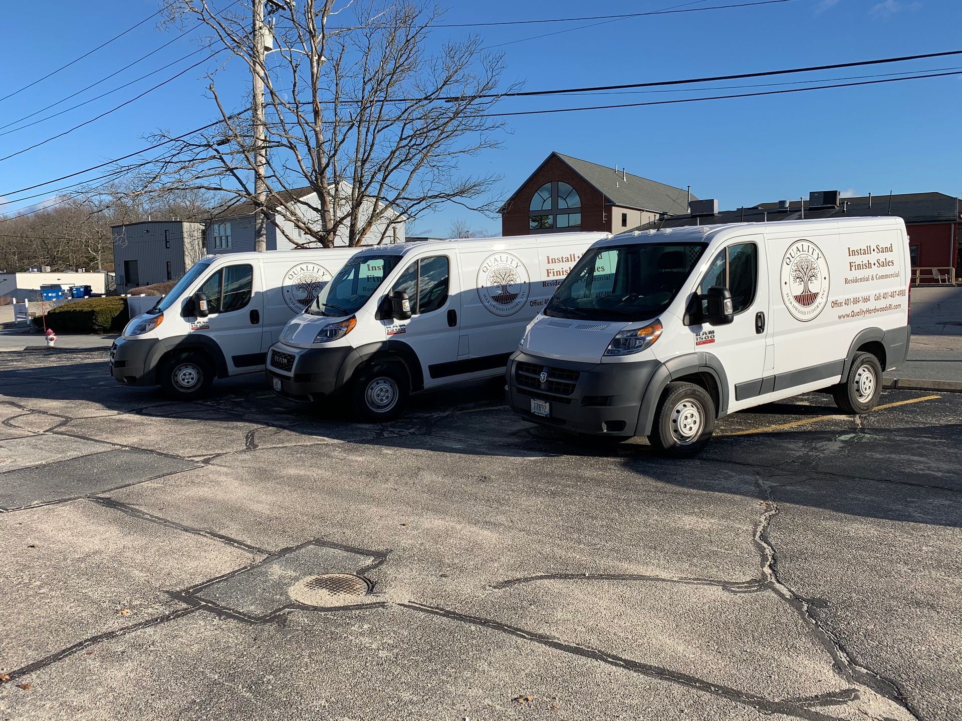 Three white work vans parked on asphalt in front of a building under a clear blue sky.