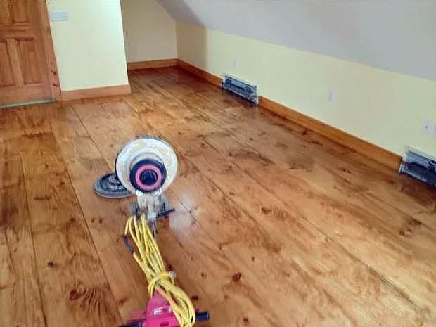 A floor sander on newly refinished wooden floorboards in a room with beige walls.