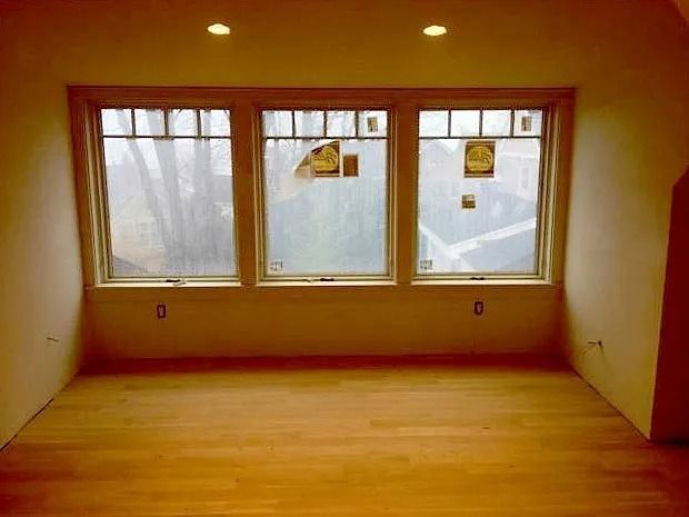Empty room with wood floor, three windows, and tan walls.
