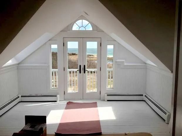 Bright attic room with white walls, ocean view, French doors, and a red yoga mat.