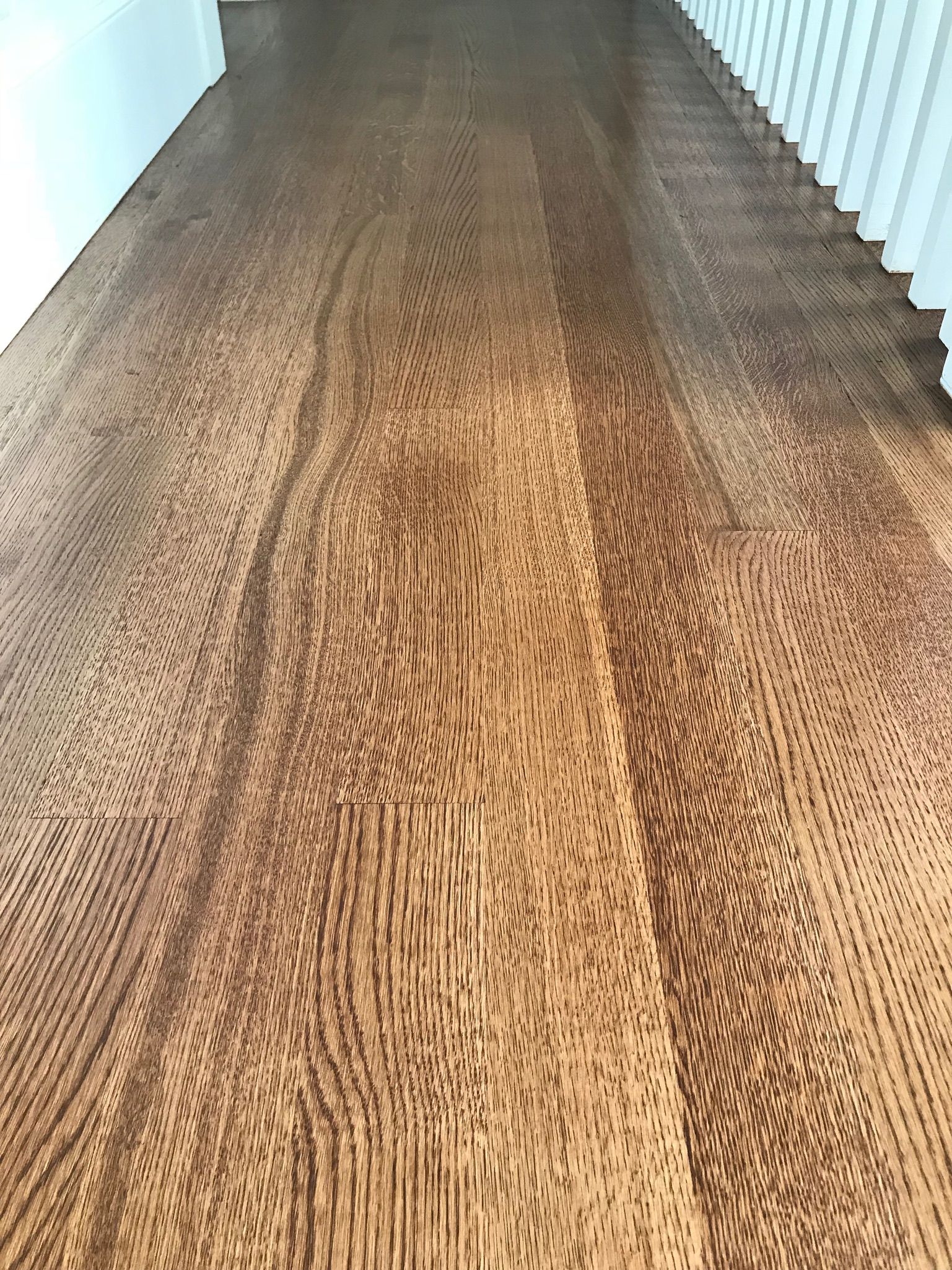 Brown hardwood floor with unique wavy grain pattern, next to white trim and railing.