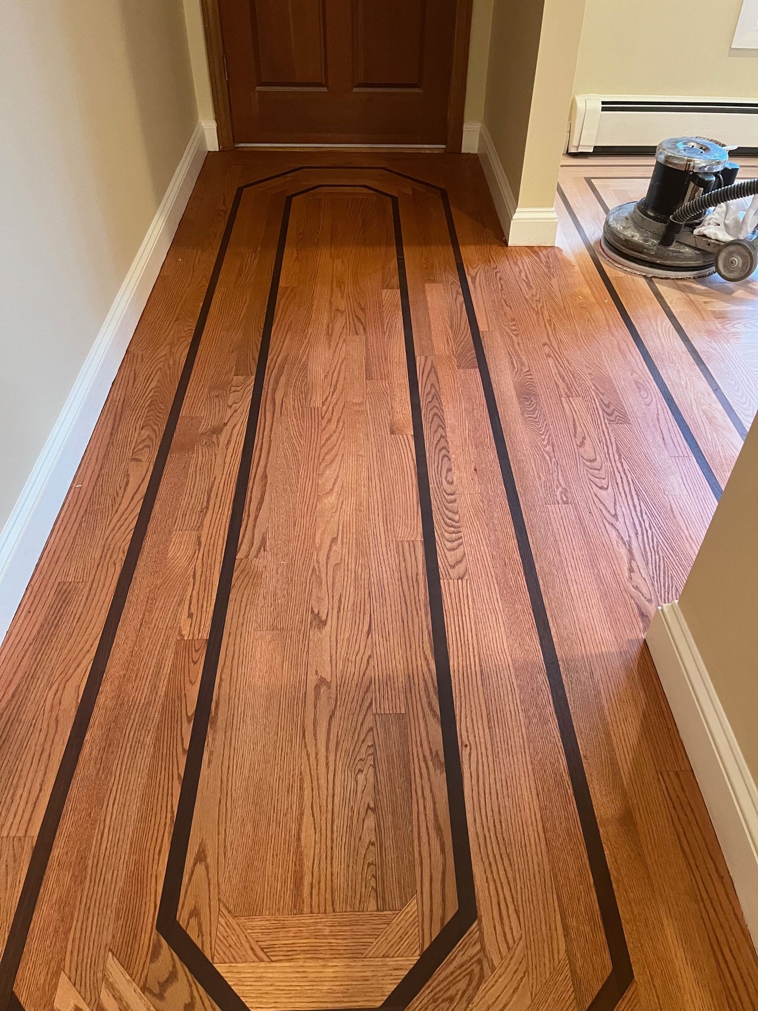 Wooden floor with dark border, door in background, floor sander in use.