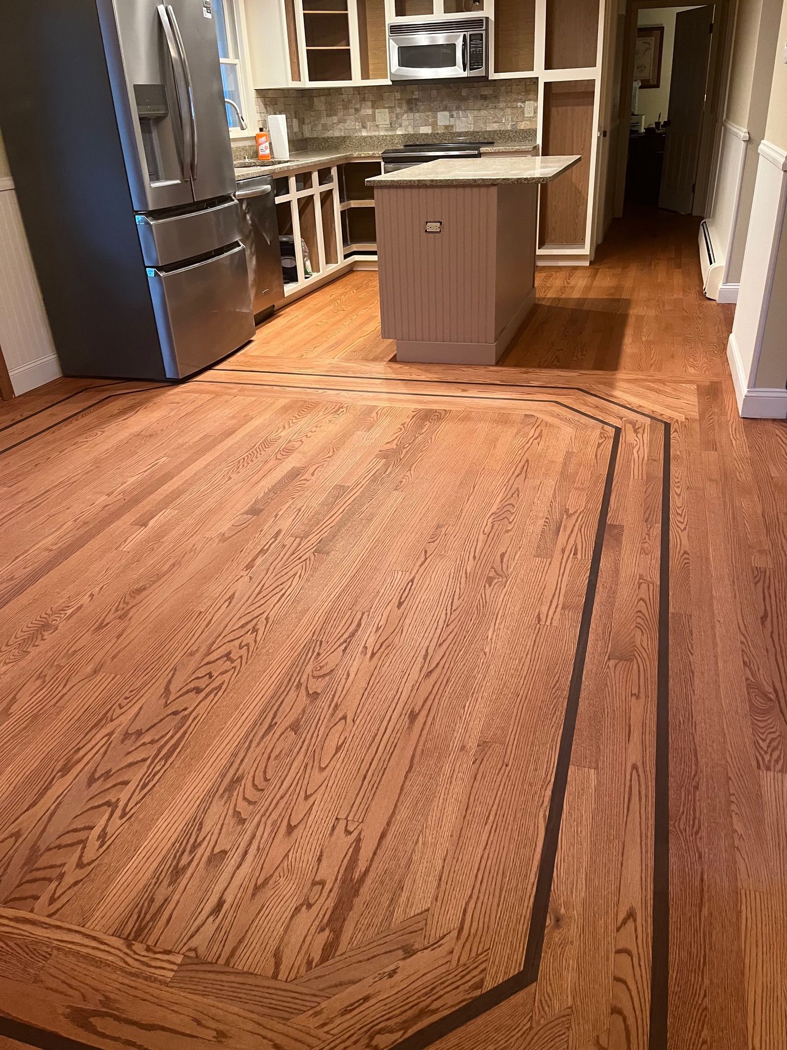 Wooden kitchen floor with a dark border, stainless steel appliances, and a central island.