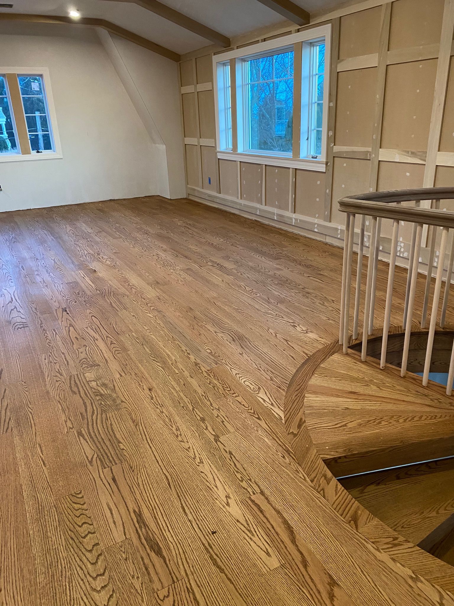Hardwood floor in an empty room with a window, and stairwell.