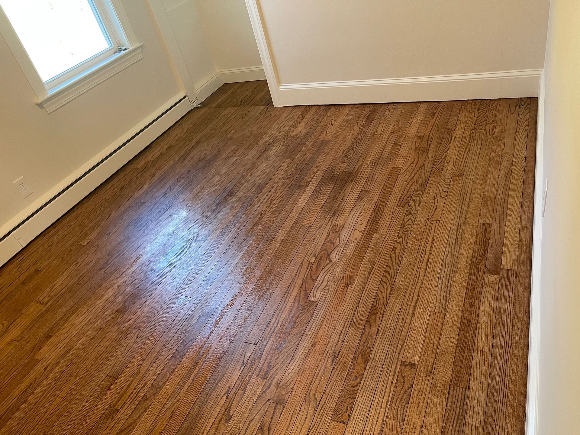 Hardwood floor in a room with white baseboards and a window.