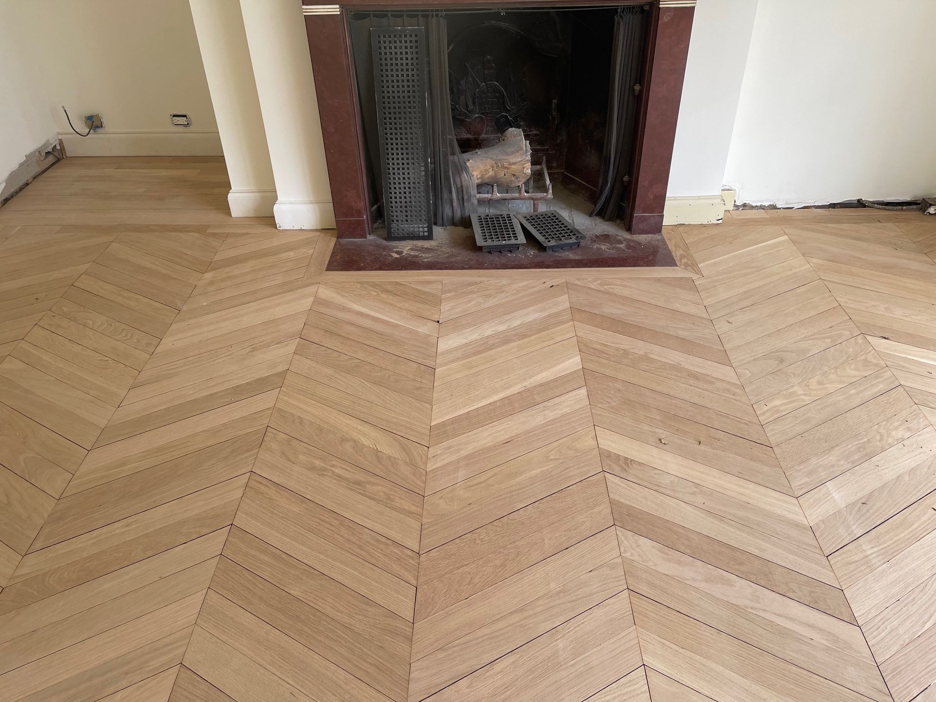 Wooden chevron-patterned floor in a room with a fireplace and white walls.