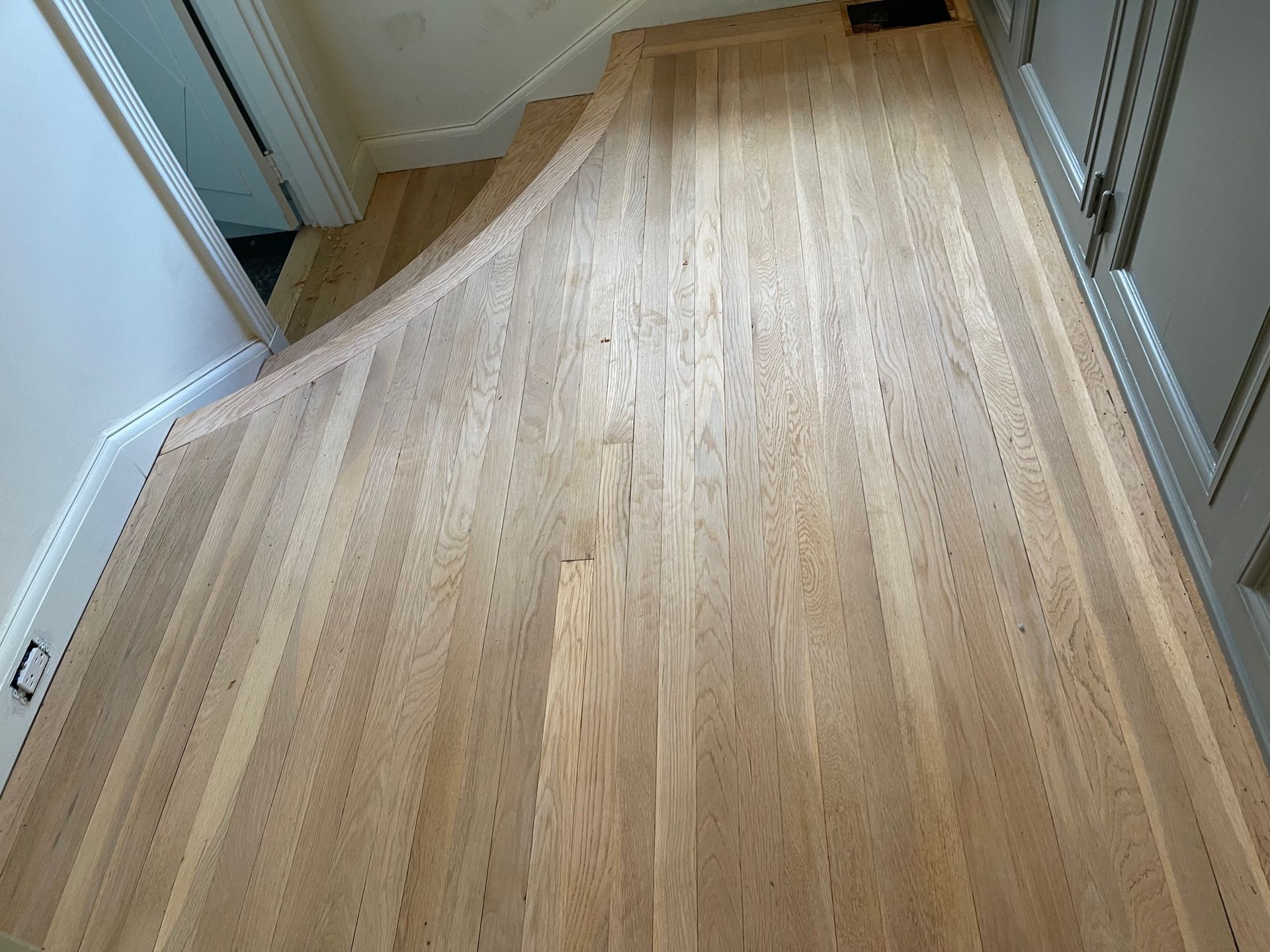 Light wood flooring in a hallway with a curved entryway.