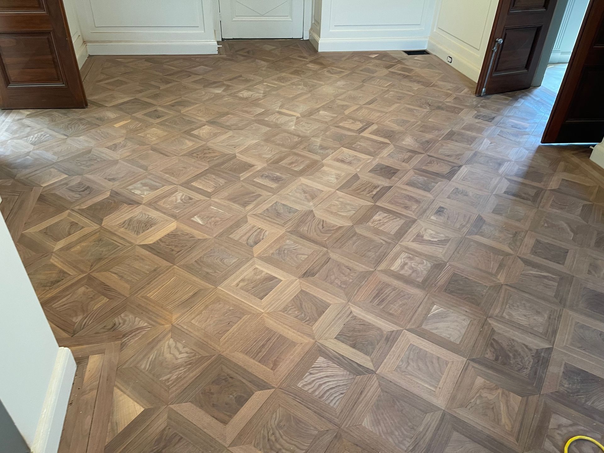 Wooden parquet flooring in a geometric pattern, in a room with doorways and white walls.